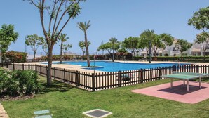 Una piscina circondata da una recinzione in legno, con palme e un'area verde sullo sfondo.