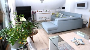 A modern living room with a grey sofa, a glass coffee table, and a potted plant with yellow flowers. - Apartment with balcony in a quiet, sunny location on the outskirts of Saxon Switzerland (Sebnitz)