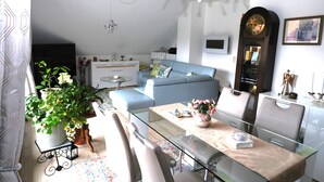 A modern living room with a glass dining table, a blue sofa, and a large wall clock. - Apartment with balcony in a quiet, sunny location on the outskirts of Saxon Switzerland (Sebnitz)