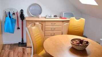 Een eetruimte met een ronde tafel, gele stoelen, een mand met appels en een dakraam erboven.