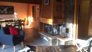 Ein gemütliches Blockhaus-Interieur mit Kamin aus Stein, Holzwänden, einem Essbereich und einem blauen Sessel.