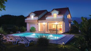 Una casa de dos pisos con piscina, mobiliario exterior y una entrada bien iluminada.