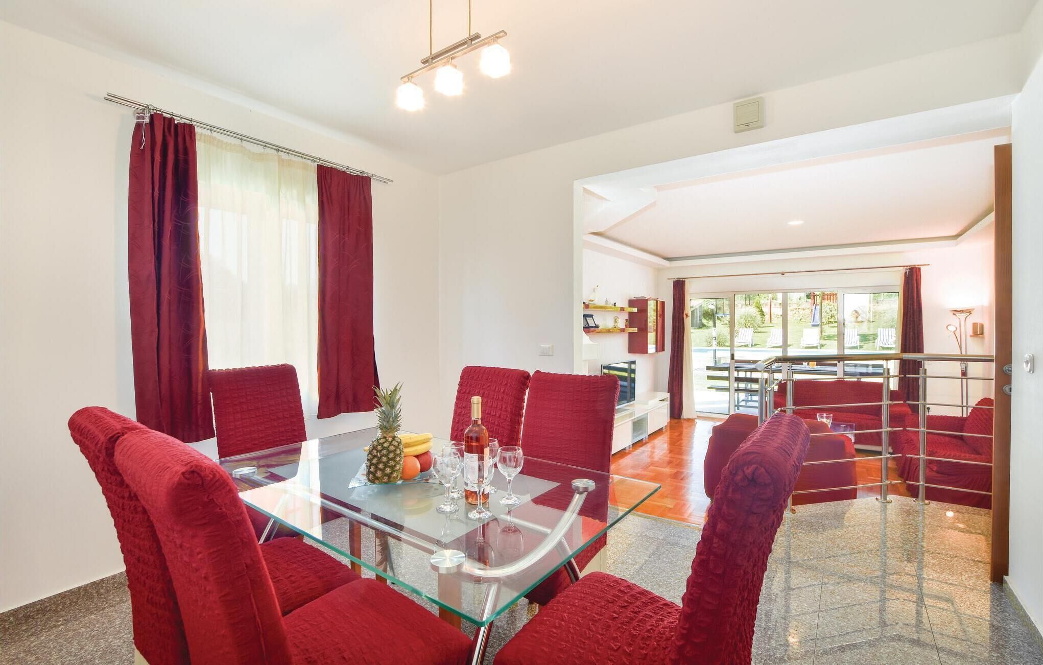 A dining area with a glass table, red upholstered chairs, and a view of the outdoor patio.