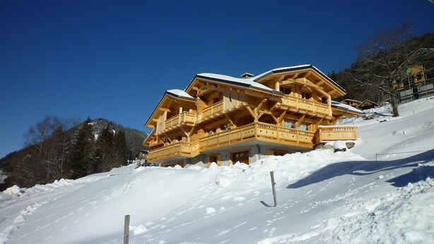 A wooden chalet with multiple balconies and a snow-covered roof, situated on a snowy slope. - Upscale chalet not far from the ski slopes  (Châtel)