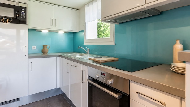 A modern kitchen with white cabinets, a stainless steel range hood, a built-in oven, and a window with a view of greenery outside. - Charming 3* apartment, near slopes, wood stove, garage, WIFI (La Clusaz)