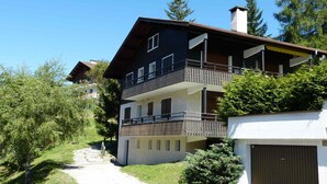 A multi-story building with a balcony, surrounded by greenery and trees. - Charming 3* apartment, near slopes, wood stove, garage, WIFI (La Clusaz)