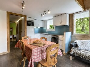 A compact kitchen with a dining area, a bed, and a window with a view of greenery.