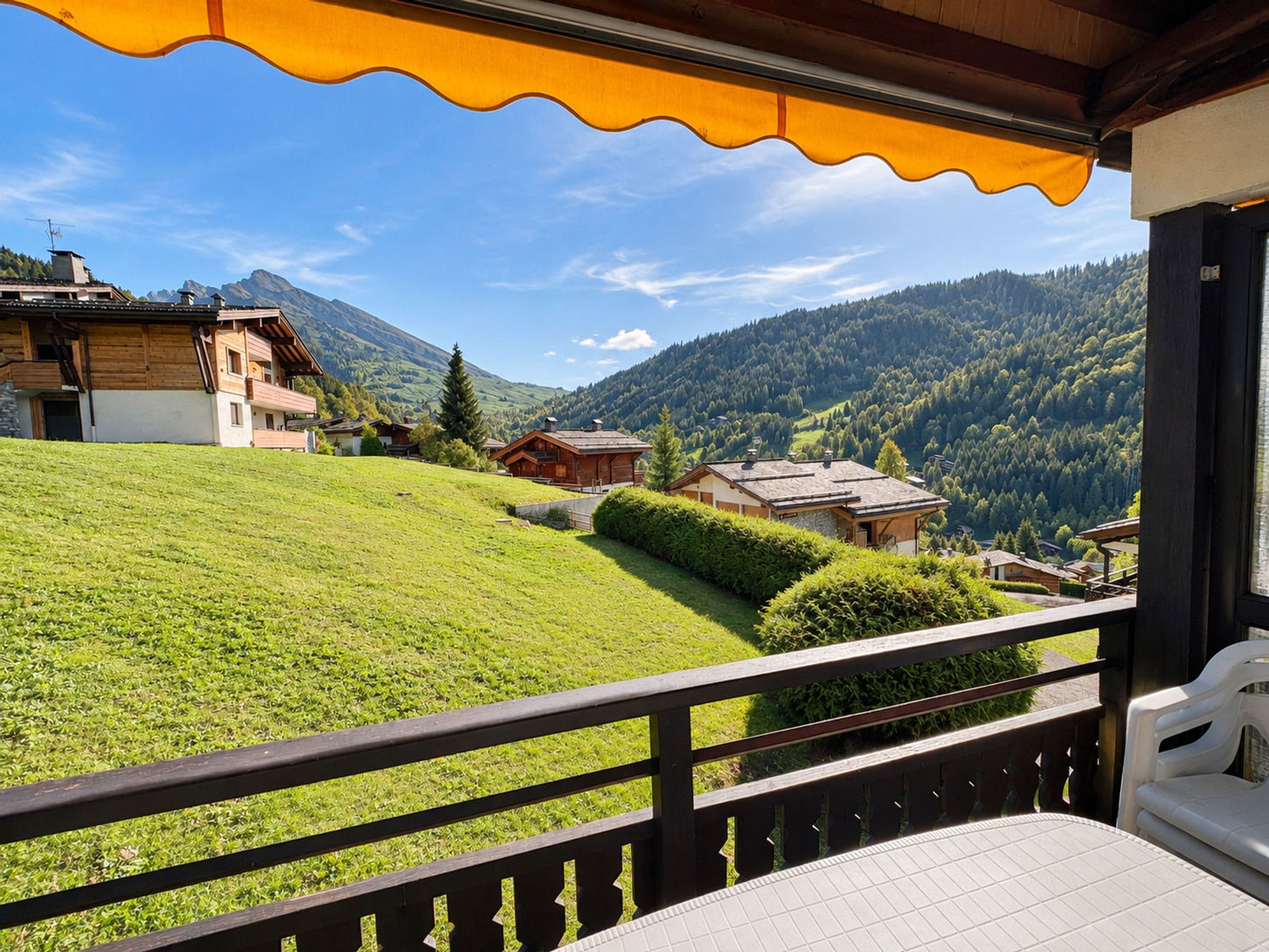 Un balcon offrant une vue sur une colline verdoyante, des bâtiments en bois et une chaîne de montagnes.