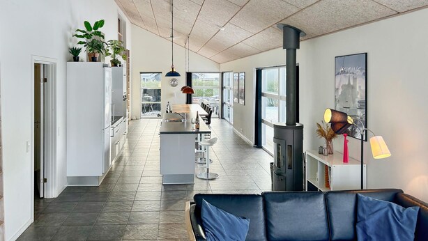Una cocina moderna con una isla central, un comedor con un sofá de cuero negro y un amplio ventanal con vistas al exterior.