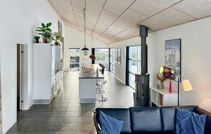 A modern kitchen with a central island, a dining area with a black leather couch, and a large window providing a view of the outdoors. - Stunning home in Sydals with sauna (Sydals)
