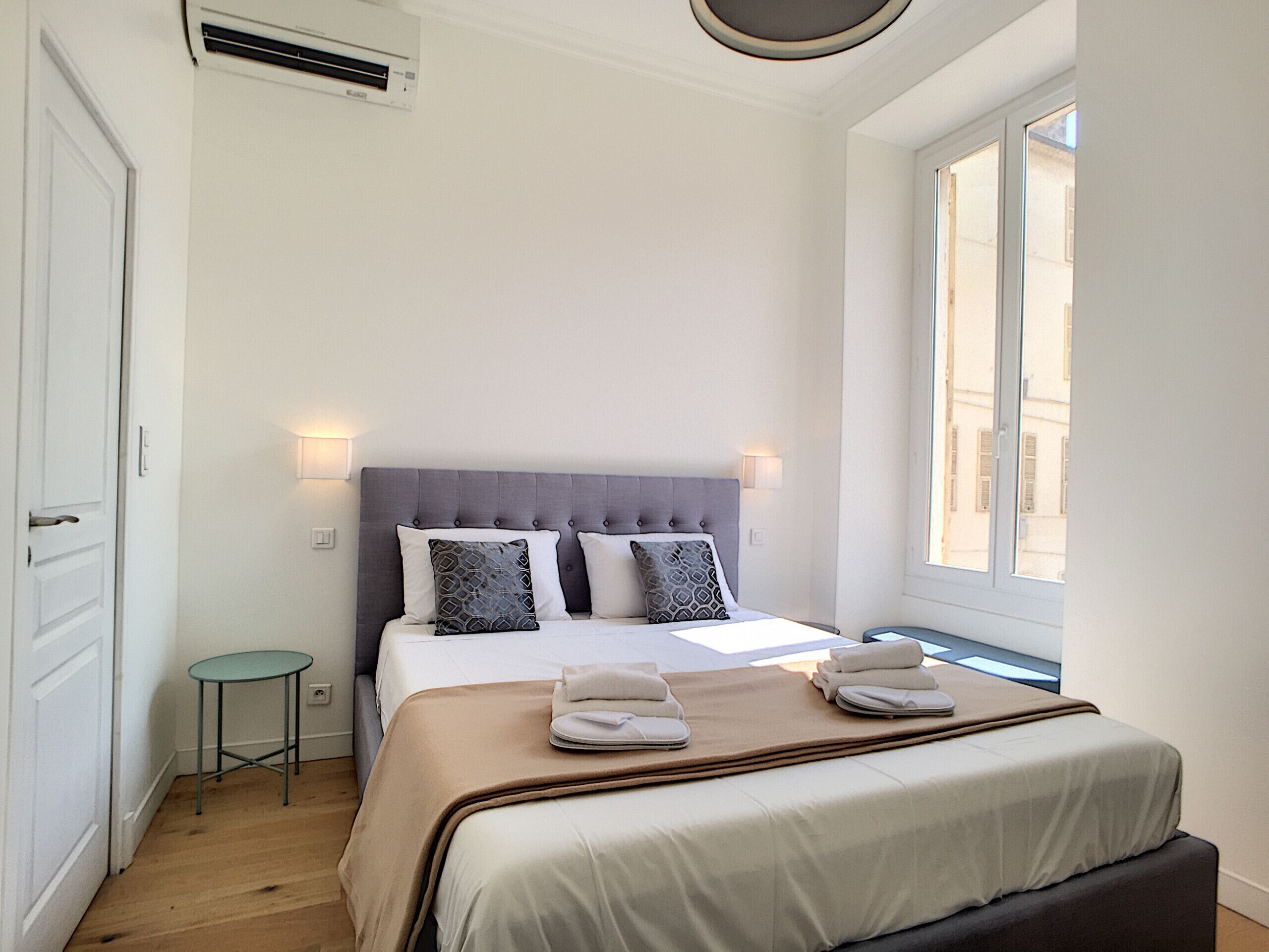A bedroom with a bed, bedside lamps, a small table, and a window.