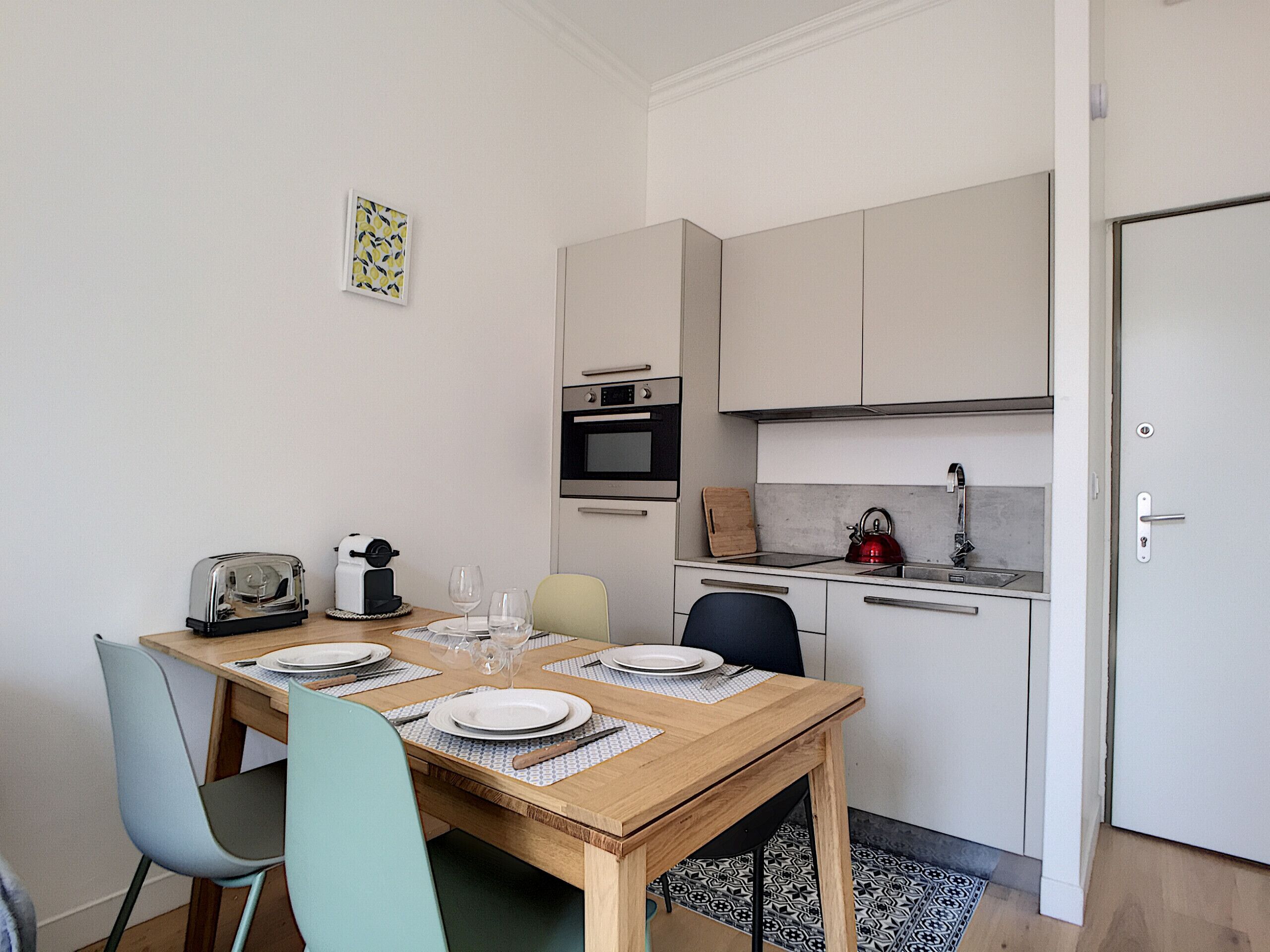 Una cocina compacta con una mesa de comedor lista para dos personas, un tostador, una tetera y un microondas.