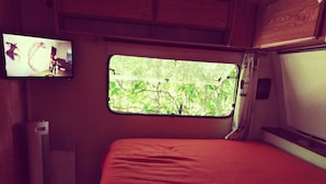 A small room with a bed, a window with a view of trees, a wall-mounted TV, and a heater. - Chalet in campingWell placed quietly, next to the pool, beautiful terrace in the shade (Sigean)