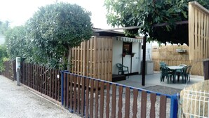 A fenced outdoor area with a wooden structure, a table with chairs, and a small garden. - Chalet in campingWell placed quietly, next to the pool, beautiful terrace in the shade (Sigean)