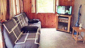 A wooden cabin interior with a sofa, television, and a small shelf with items. - Chalet in campingWell placed quietly, next to the pool, beautiful terrace in the shade (Sigean)