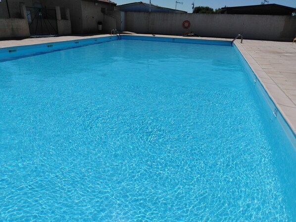 A rectangular swimming pool with clear blue water, surrounded by a tiled deck and a low wall.