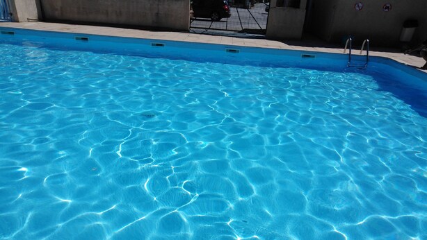 A clear blue swimming pool with a metal ladder and a concrete edge. - Chalet in campingWell placed quietly, next to the pool, beautiful terrace in the shade (Sigean)