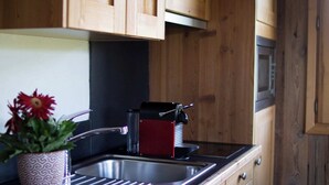 Uma cozinha com armários de madeira, uma pia de aço inoxidável, uma chaleira vermelha e um vaso com planta.