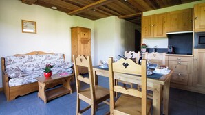Um quarto acolhedor com teto de madeira, um sofá com capa estampada, uma mesa de jantar de madeira com cadeiras e uma cozinha com armários e eletrodomésticos de madeira.