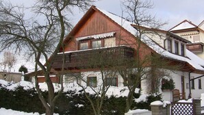 A two-story house with a wooden balcony, surrounded by snow-covered trees and a fence. - quiet, attractive apartment with 2 bedrooms (Meiningen OT Walldorf)