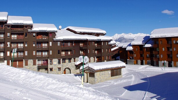 Een gebouwcomplex bedekt met sneeuw, met meerdere balkons en een skipiste op de voorgrond.