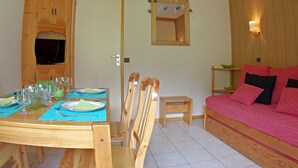 Een kamer met een houten eettafel voor vier personen, een klein houten krukje, een roze bank en een spiegel aan de muur.