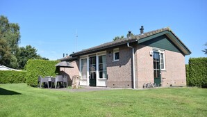 Una casa de ladrillo de dos pisos con techo verde, un patio con mobiliario exterior y un césped bien cuidado.