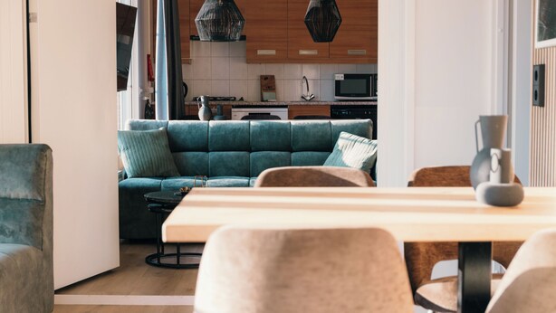 Una sala de estar moderna con un sofá color turquesa, una mesa de comedor de madera y una cocina al fondo.