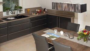 A modern kitchen with dark cabinetry, a wooden dining table, and a hanging light fixture.