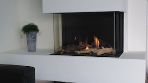 A modern fireplace with a clean, white mantel and a potted plant to the left.