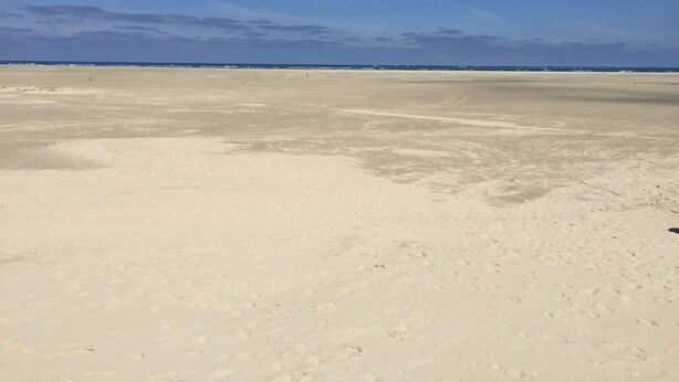 A wide, open sandy beach with a clear blue sky.