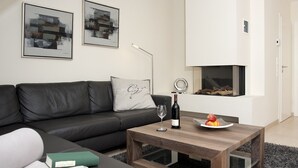 A modern living room with a black leather sofa, a wooden coffee table, a fireplace, and abstract paintings on the wall.