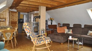 Ein gemütlicher Wohnbereich mit Holzbalkendecke, einer Couch, einem Schaukelstuhl und einem Esstisch.