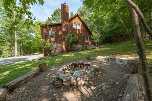 Escape to a secluded cabin surrounded by lush greenery, featuring a cozy fireplace and outdoor fire pit.