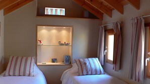 A cozy room with two beds, a shelf with decorative items, and a window with curtains.