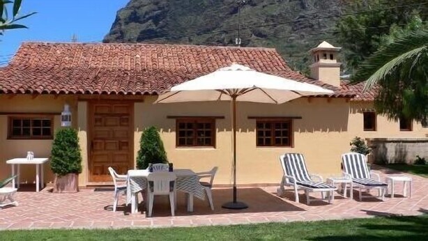 A building with a tiled roof, a wooden door, and a small tower. There are outdoor tables and chairs, and a large umbrella.