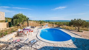 Une piscine entourée de chaises longues et d’un mur de pierre, avec une terrasse en pierre et une vue sur la campagne.