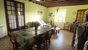 Comedor con una mesa preparada para cuatro personas, sillas de madera, una araña y una ventana con cortinas.