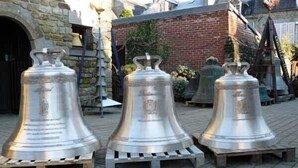 Tres campanas metálicas grandes sobre soportes de madera al aire libre.