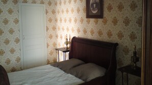 Camera da letto con carta da parati a motivi floreali, un letto di legno, un comodino con una lampada e un quadro appeso al muro.