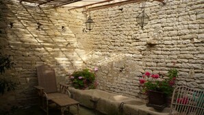 Un cortile con pareti in pietra, sedie in vimini e piante in vaso.