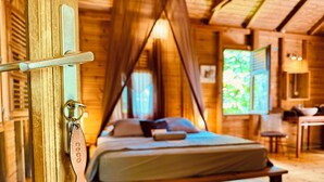 A wooden cabin bedroom with a bed, a desk, and a window.