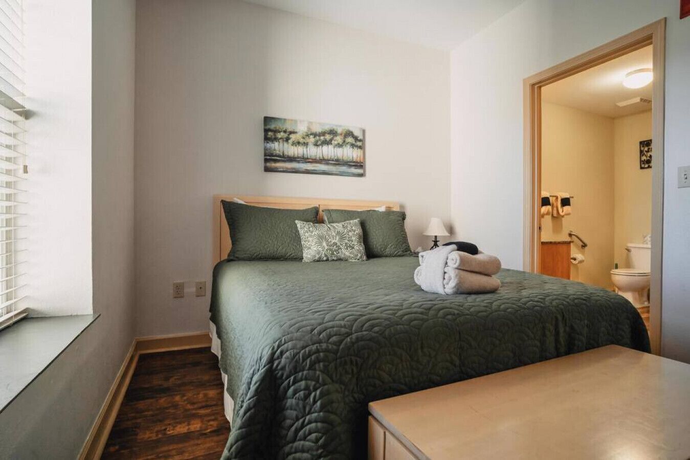 Une chambre à coucher bien rangée, avec un lit, une table de chevet, un tableau au mur et une vue sur la salle de bain.