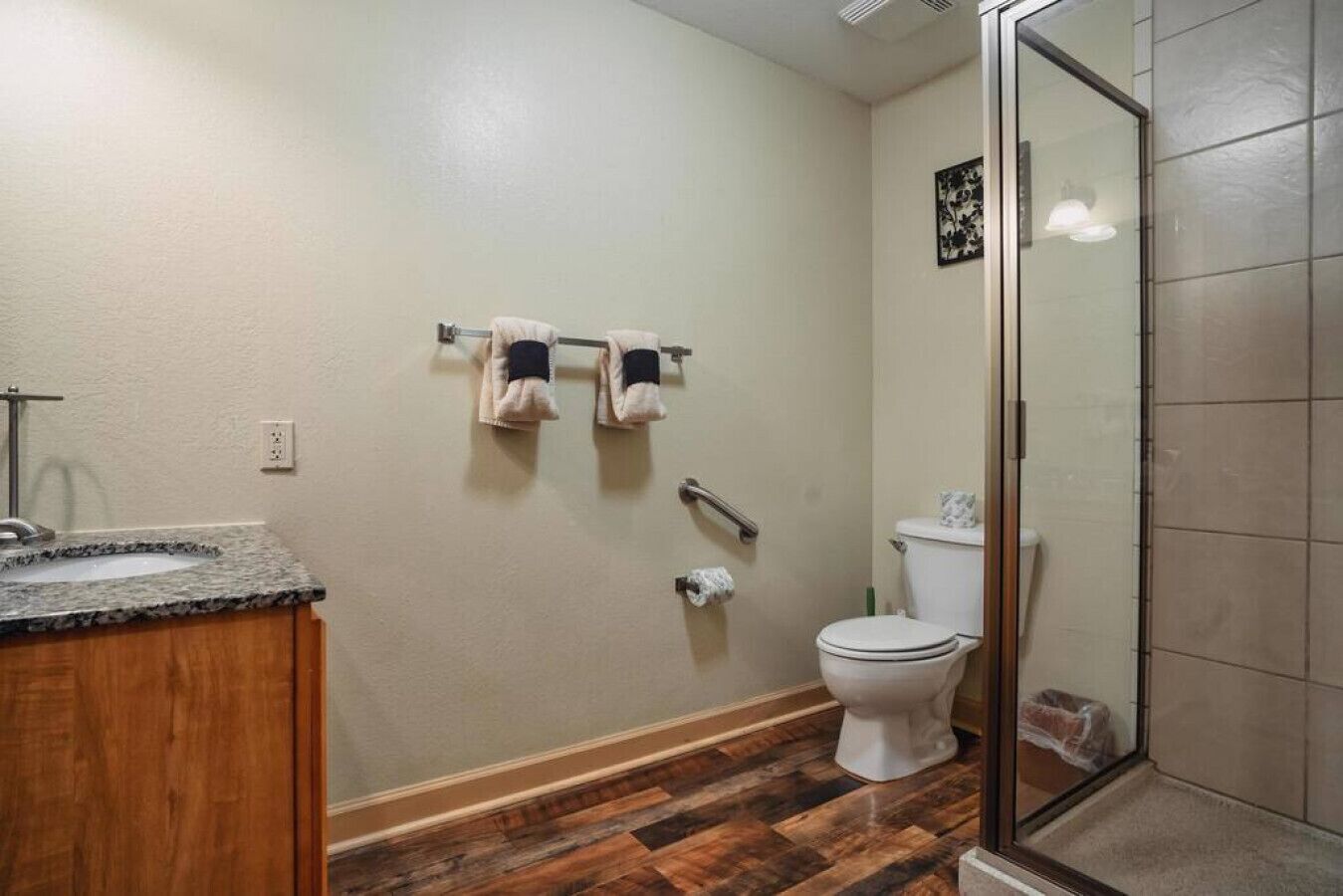 A bathroom with a granite countertop sink, a toilet, and a glass shower enclosure.