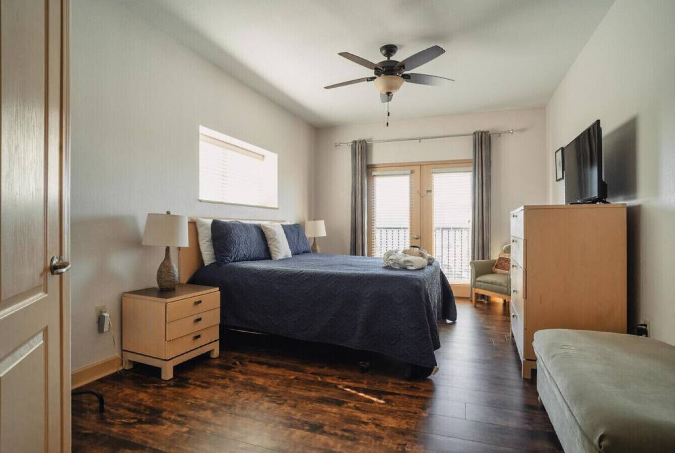 A bedroom with a bed, bedside tables, a ceiling fan, a television, and a window with curtains.