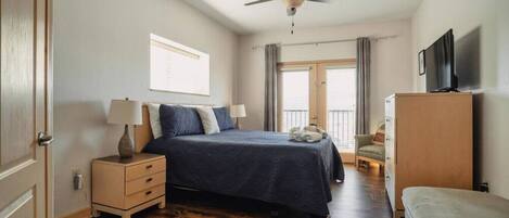 A bedroom with a bed, bedside tables, a ceiling fan, a television, and a window with curtains.