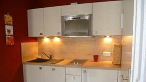 A compact kitchen with white cabinets, a stainless steel oven, a sink, and a red cup on the countertop. - Apartment stylish + cozy, in 3 minutes at the sea or in the center :) with parking space (Rostock)