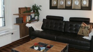 A living room with a black leather sofa, a wooden coffee table with a magazine, a bookshelf with books and a plant, and a wall with framed pictures. - Apartment stylish + cozy, in 3 minutes at the sea or in the center :) with parking space (Rostock)