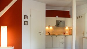 A compact living space with a kitchenette, a tufted ottoman, and a door leading to another room. - Apartment stylish + cozy, in 3 minutes at the sea or in the center :) with parking space (Rostock)