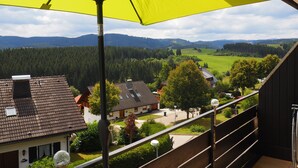 Un balcon agrémenté d’un parasol jaune, donnant sur un quartier résidentiel avec des maisons et un paysage boisé.